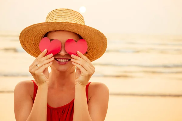 Belleza sorprendida modelo de moda chica con corazón de San Valentín en forma de mano en la playa. Retrato de amor mujer joven en sombrero de paja y tarjeta en su mano El regalo del 14 de febrero del Día de San Valentín. — Foto de Stock