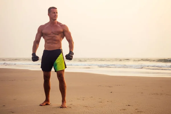 Snygg ung muskulös manlig modell gör träningen stretching värma upp på stranden sommaren. sexig atlet ABS och perfekt kropp i tropiska paradis Shore Sunset — Stockfoto