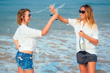 İki güzel kız arkadaş sahilde şampanya içer.