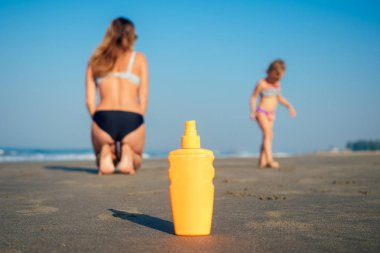 Sahilde güneş kremi sürmüş turuncu şişe. Anne ve kızı.