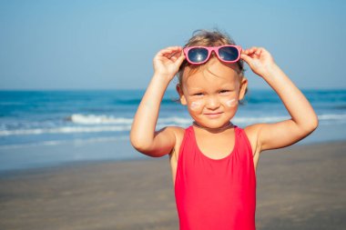 Sevimli küçük kız sahilde güneş gözlüğü takıyor.