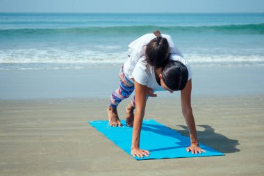 Neşeli kız ve anne kumsalda yoga yapıyor.