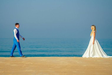 Şık bir takım elbise içinde yakışıklı bir damat ve sahilde gelinlik giymiş güzel bir gelin. Kumsalda şık ve zengin bir düğün töreni konsepti. kopyalama alanı