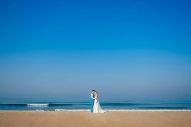 Şık bir takım elbise içinde yakışıklı bir damat ve sahilde gelinlik giymiş güzel bir gelin. Kumsalda şık ve zengin bir düğün töreni konsepti. kopyalama alanı