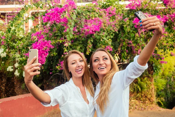 Zwei Frauen machen Selfie vor dem Hintergrund einer Blumenwand — Stockfoto