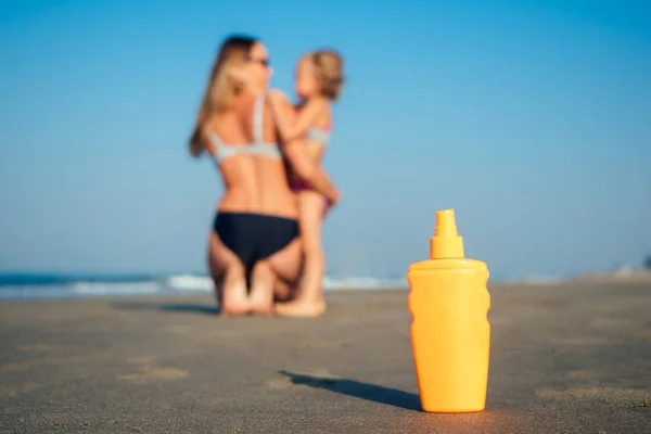 orange bottle with sunscreen on the beach in the background mother and daughter