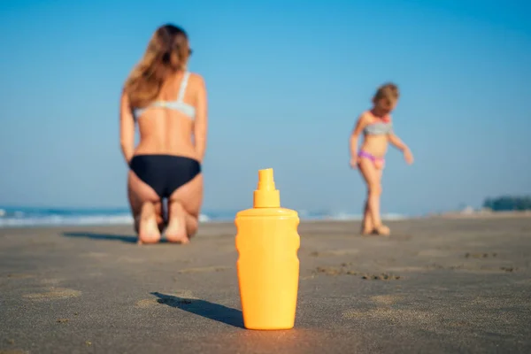 Botella naranja con protector solar en la playa en el fondo madre e hija — Foto de Stock