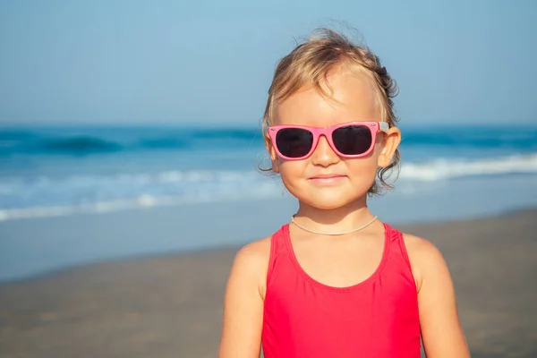 Очаровательная маленькая девочка надевает солнечные очки на пляже — стоковое фото