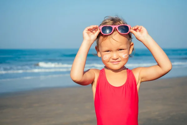 Очаровательная маленькая девочка надевает солнечные очки на пляже — стоковое фото