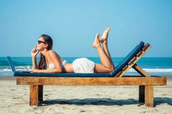 Güzel ve seksi genç bir kadın deniz laptopuyla güverte sandalyesinde uzanıyor ve dinleniyor. Otelde dizüstü bilgisayarı olan serbest çalışan bir kadın.