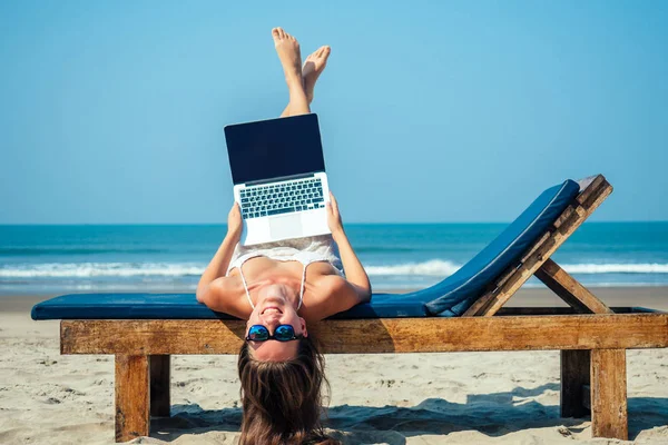 Güzel ve seksi genç bir kadın deniz laptopuyla güverte sandalyesinde uzanıyor ve dinleniyor. Otelde dizüstü bilgisayarı olan serbest çalışan bir kadın.