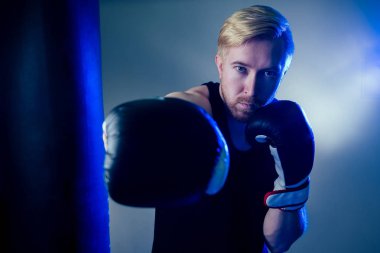 Genç bir erkek boksör spor salonunda spor yapıyor. Boksör, siyah arka planda boks eldivenleri. Adam saldırıyor