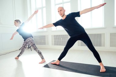 Yoga yapan bir adam ve bir kadın stüdyoda. Yoga dersinde sabah kuşları. Takım spor salonunda çalışıyor. Yoga sınıfında çift yoga.