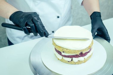 Siyah eldivenli ve beyaz üniformalı pastacı masanın üstüne krema koyuyor. Şekerleme, pasta, yemek..