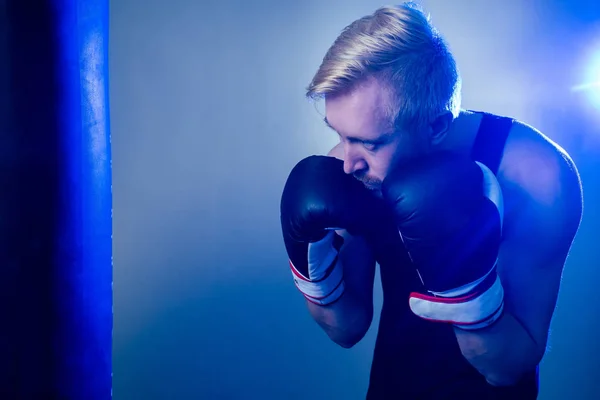 Um jovem pugilista está a praticar desporto no ginásio. boxeador, luvas de boxe num fundo escuro. homem ataca — Fotografia de Stock