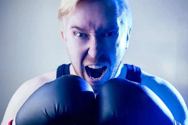 Egy portré egy dühös és gonosz férfi bokszolóról, aki sportol a tornateremben. bokszoló és bokszkesztyű sötét háttérrel. A férfi lecsap. kötés a kezeken — Stock Fotó