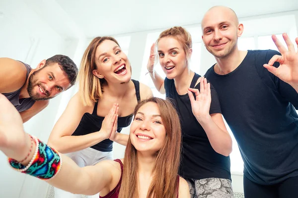a happy group of people from man and woman practicing yoga in the studio and making selfies on the phone. groups of meditation and support in the yoga class. men and women have fun