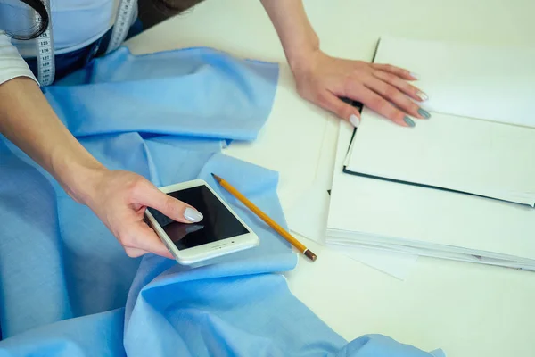 A costureira segura o telefone na mão. o alfaiate cose na máquina de costura. dressmaker digita o texto no telefone . — Fotografia de Stock