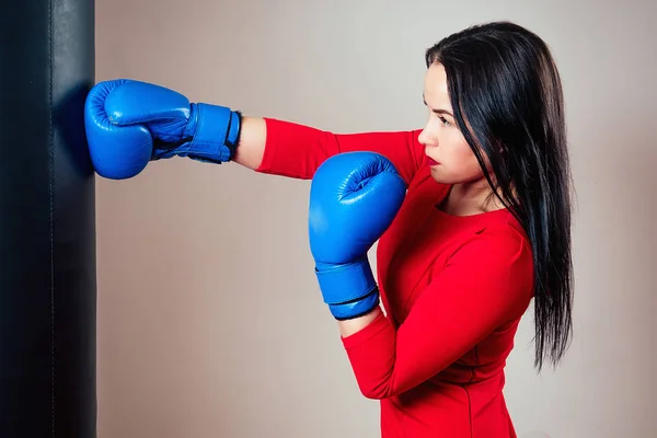 Egy gyönyörű barna nő portréja, aki bokszkesztyűvel a kezén edz a tornateremben. Sportoló smink piros rúzzsal és ruha boksz a tornateremben. a női hatalom és feminizmus fogalma — Stock Fotó