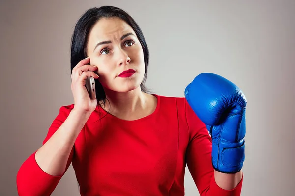 Porträtt av en vacker brunett kvinna med boxningshandskar och en telefon i armarna i gymmet. idrottare med makeup rött läppstift boxning. kvinnlig makt, feminism — Stockfoto