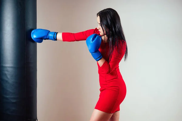 Porträtt av en vacker brunett kvinna som tränar med boxningshandskar på händerna i gymmet. Idrottare med smink rött läppstift och klänning boxning i gymmet. Begreppet kvinnlig makt och feminism — Stockfoto