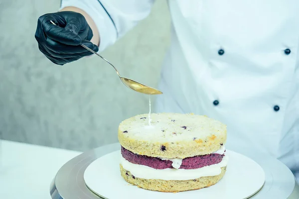 confectioner in black gloves and white work uniforms puts cream on the cake on the table. confectioner, cake, cooking.