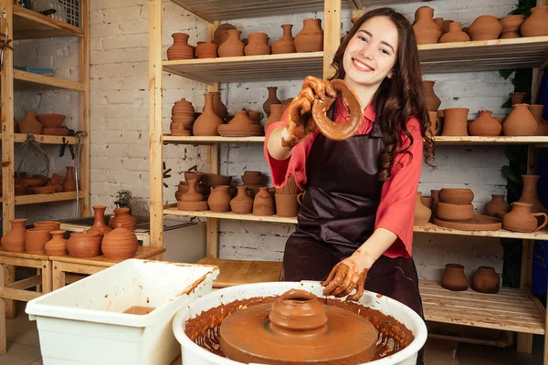 Uma mulher jovem e alegre esculpe de barro. O oleiro trabalha em uma oficina de cerâmica com argila. o conceito de mestria de cerâmica e criatividade — Fotografia de Stock