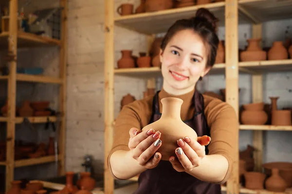 一个年轻而快乐的女人拿着一个陶土花瓶。 陶工在一个用粘土做的陶器车间里工作. 陶瓷的掌握和创造力的概念 — 图库照片