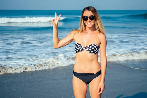 Hermosa mujer de pie en un traje de baño y con gafas de sol en la playa — Foto de Stock