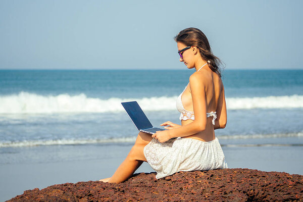 portrait of a young and beautiful freelancer girl running on the beach with a laptop. woman businessman on vacation. concept of freelancing and work