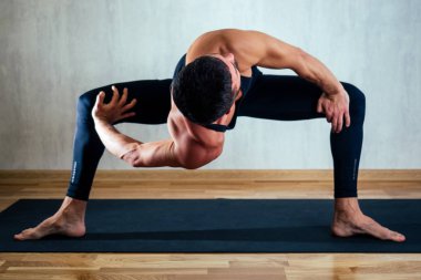 Koyu renk spor giyimli bir adam karanlık arka planda yoga yapıyor. Asana yoga minderlerinin üzerinde yerde. Konsantrasyon ve bedenin ele geçirilmesi kavramı