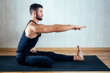 Koyu renk spor giyimli bir adam karanlık arka planda yoga yapıyor. Asana yoga minderlerinin üzerinde yerde. Konsantrasyon ve bedenin ele geçirilmesi kavramı