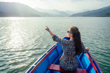 Güzel ve genç bir kadın dağların arkasındaki gölde bir teknede. Doğadaki doğa aktiviteleri ve turizm kavramı. Nepal Himalayaları 'nda yürüyüş