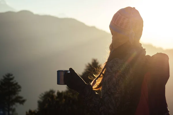 A beautiful and active woman holds a cup with a hot drink in her hands. the concept of active recreation and tourism in the mountains. trekking in Nepal Himalayas