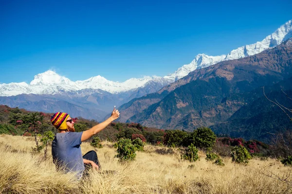 Молодой человек с рыжей бородой и рюкзаком в горах делает селфи. концепция активного отдыха и туризма в горах. Весной в Непале — стоковое фото