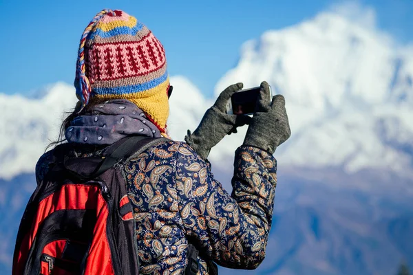 Uma jovem turista com uma mochila para caminhadas e um chapéu de malha fotografando paisagens nas montanhas do Himalaia. conceito de trekking nas montanhas — Fotografia de Stock