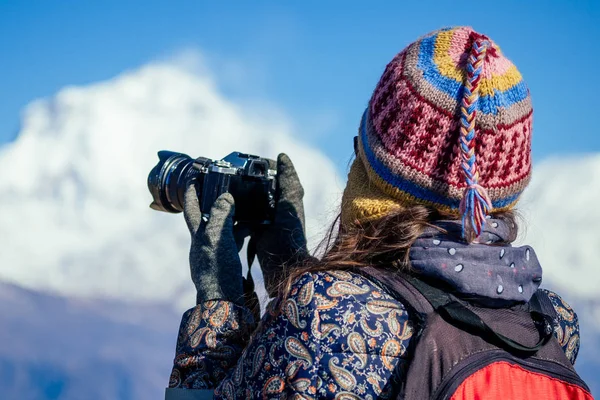 Uma jovem turista com uma mochila para caminhadas e um chapéu de malha fotografando paisagens nas montanhas do Himalaia. conceito de trekking nas montanhas — Fotografia de Stock