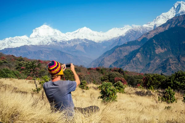 Молодой турист с рюкзаком и вязаной кепкой, фотографирующий пейзажи и делающий селфи в горах Гималаев. треккинг концепция в горах — стоковое фото