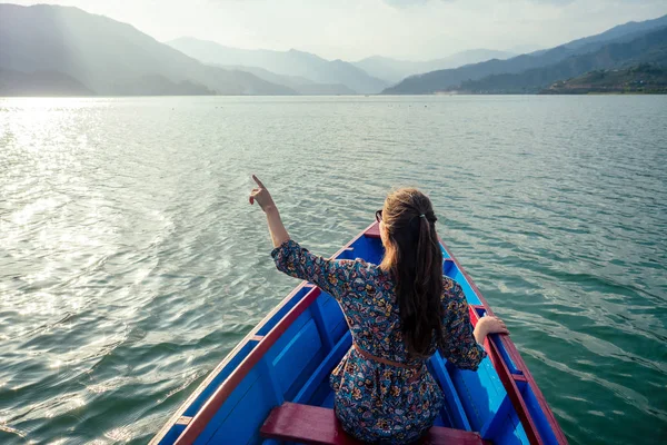Güzel elbiseli genç kadın turist tekneyle gölde yüzüyor ve dağların manzarasının tadını çıkarıyor. Açık hava aktiviteleri konsepti. arka plan