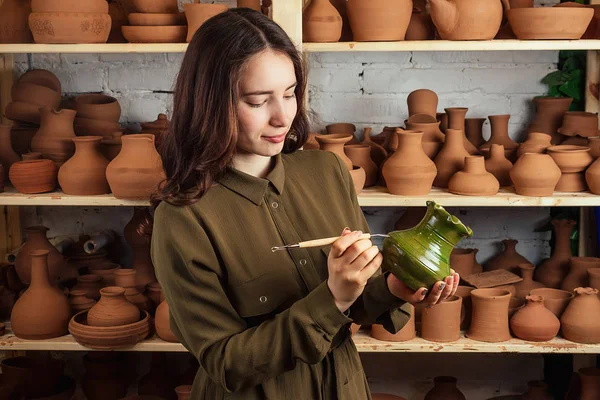 a woman holding a vase of clay in a pottery workshop near the rack with pots and vases. a vase of clay in the hands of a master