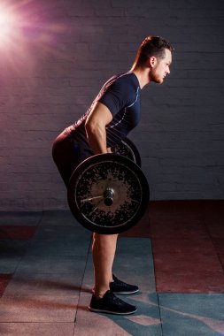 Siyah tişörtlü genç ve yakışıklı bir adam halterle meşgul.