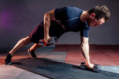 Siyah tişörtlü genç yakışıklı spor salonundaki halterlerle egzersiz yapıyor siyah tuğladan bir arka planda.