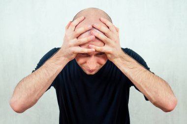 Genç kel bir adam bağırıyor ve kafasını tutarak çığlık atıyor. Erkeklerde kellik kaybı kavramı.