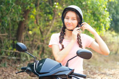 Güzel ve genç bir kadın motosiklet üzerinde otururken kaskını ilikliyor. Güvenli scooter kullanma kavramı