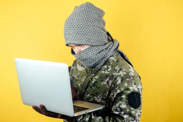 一个穿迷彩服、戴着面具的黑客的画像正在看笔记本电脑 — 图库照片