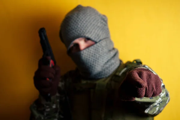 Kamuflajlı ve maskeli bir adam silah tutuyor ve parmağıyla işaret ediyor. — Stok fotoğraf