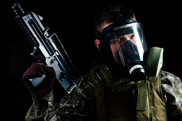 Terrorista masculino em uma máscara de gás segurando uma arma em um fundo preto — Fotografia de Stock
