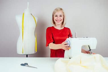 Gülümseyen kız dikiş makinesi ve beyaz arka planda sarı şeritli manken üzerinde çalışıyor.