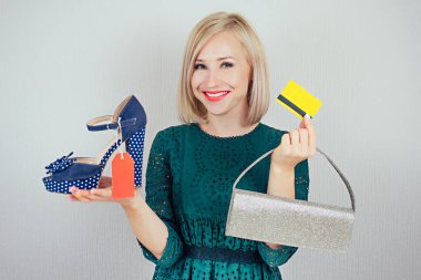 Güzel, güler yüzlü, alışveriş hastası bir kadın elinde kırmızı etiket, etiket, hesap, çanta ve elinde plastik bir kartla şık bir ayakkabı tutuyor. Mevsimlik satış ve alışveriş kavramı