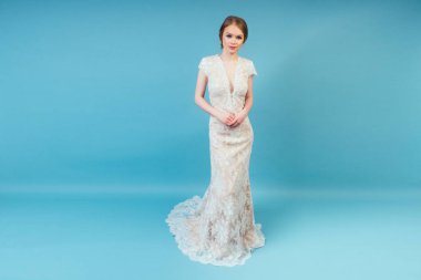 Çekici bir gülümseme modeli uzun şık, seksi beyaz bir düğünle makyajlı güzel bir kadın gelin stüdyoda mavi arka planda poz veriyor. Balo ve evlilik kavramı